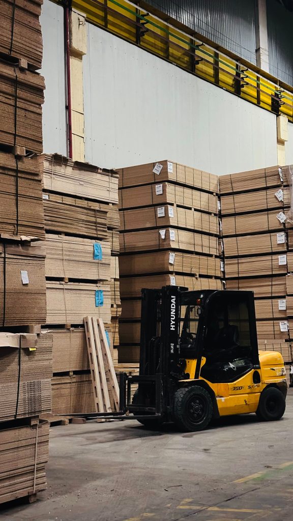 Inicio A yellow forklift organizes large stacks of cardboard boxes in a spacious warehouse.