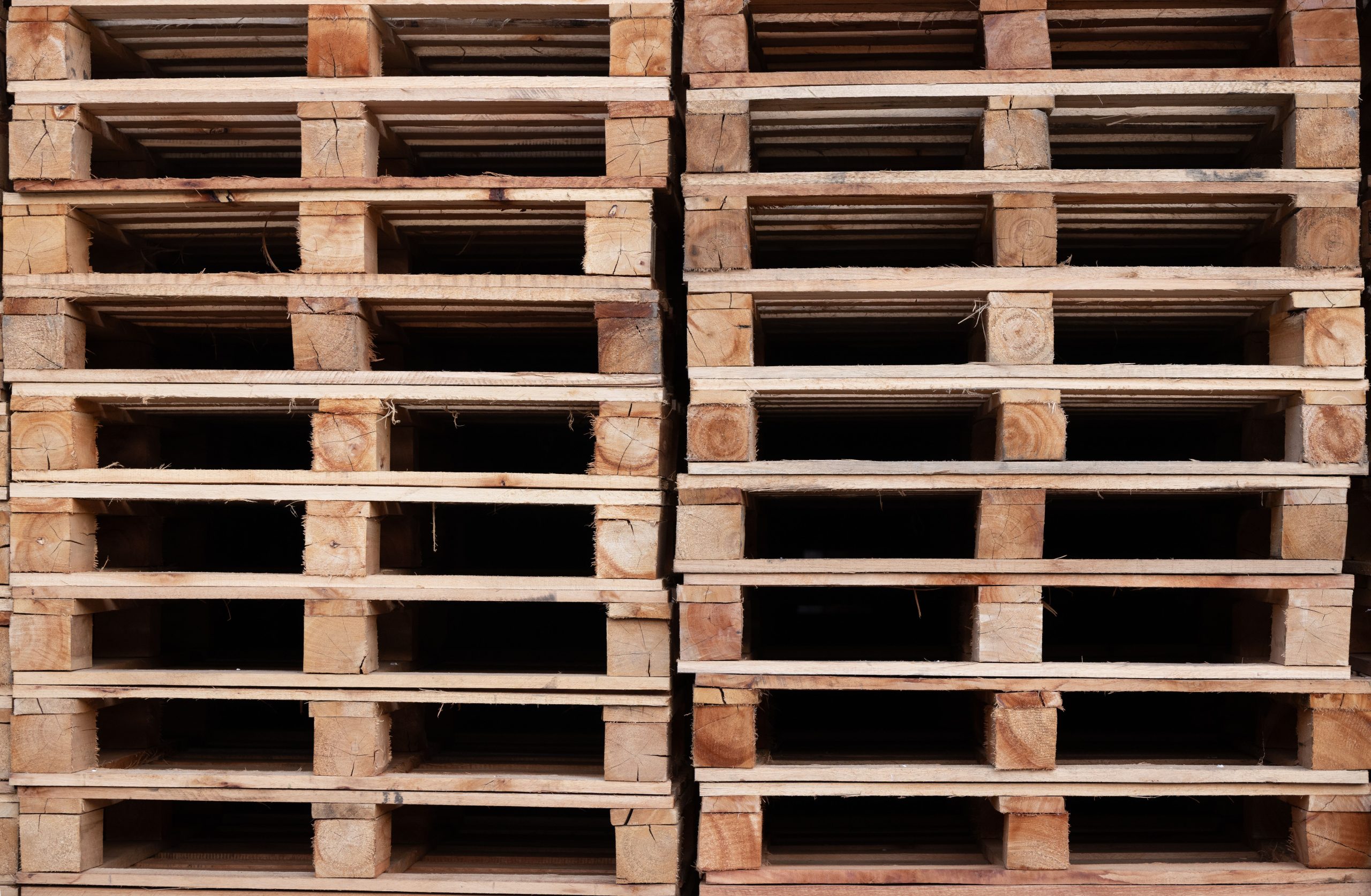 Servicios Close-up of neatly stacked wooden pallets used for shipping and storage in an industrial area.